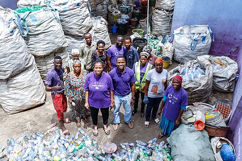 Bilikiss Adebiyi-Abiola and members of the Wecyclers team, in purple shirts, standing among sacks of collected plastic bottles