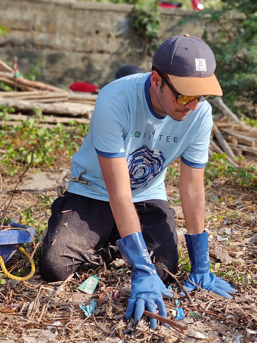 Afroz Shah in a cap and gloves, crouching to collect rubbish on the beach